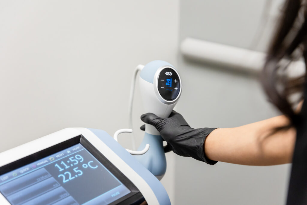 Close up of a medical provider's gloved hand holding an Exion handpeice beside the control screen for a treatment to acheive Body Contouring in Abilene.